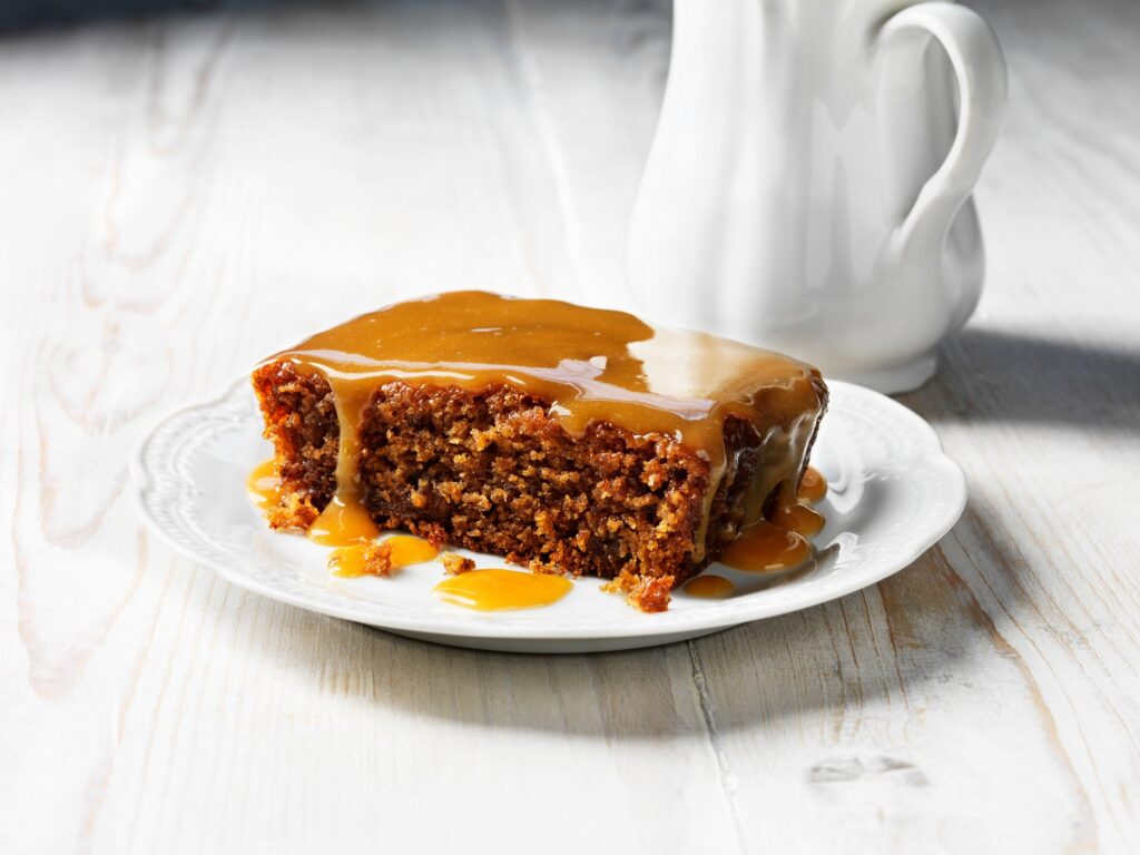Sticky toffee pudding on white plate, white jug, white wooden table